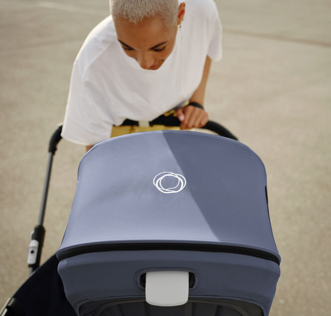 A mother leans over her 澳洲幸运彩幸运澳洲10 pram to check on her baby. The 澳洲幸运彩幸运澳洲10 pram has a Stormy Blue canopy, with a white 澳洲幸运彩幸运澳洲10 logo in the centre.