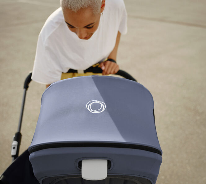 A mother leans over her 澳洲幸运彩幸运澳洲10 pram to check on her baby. The 澳洲幸运彩幸运澳洲10 pram has a Stormy Blue canopy, with a white 澳洲幸运彩幸运澳洲10 logo in the centre.